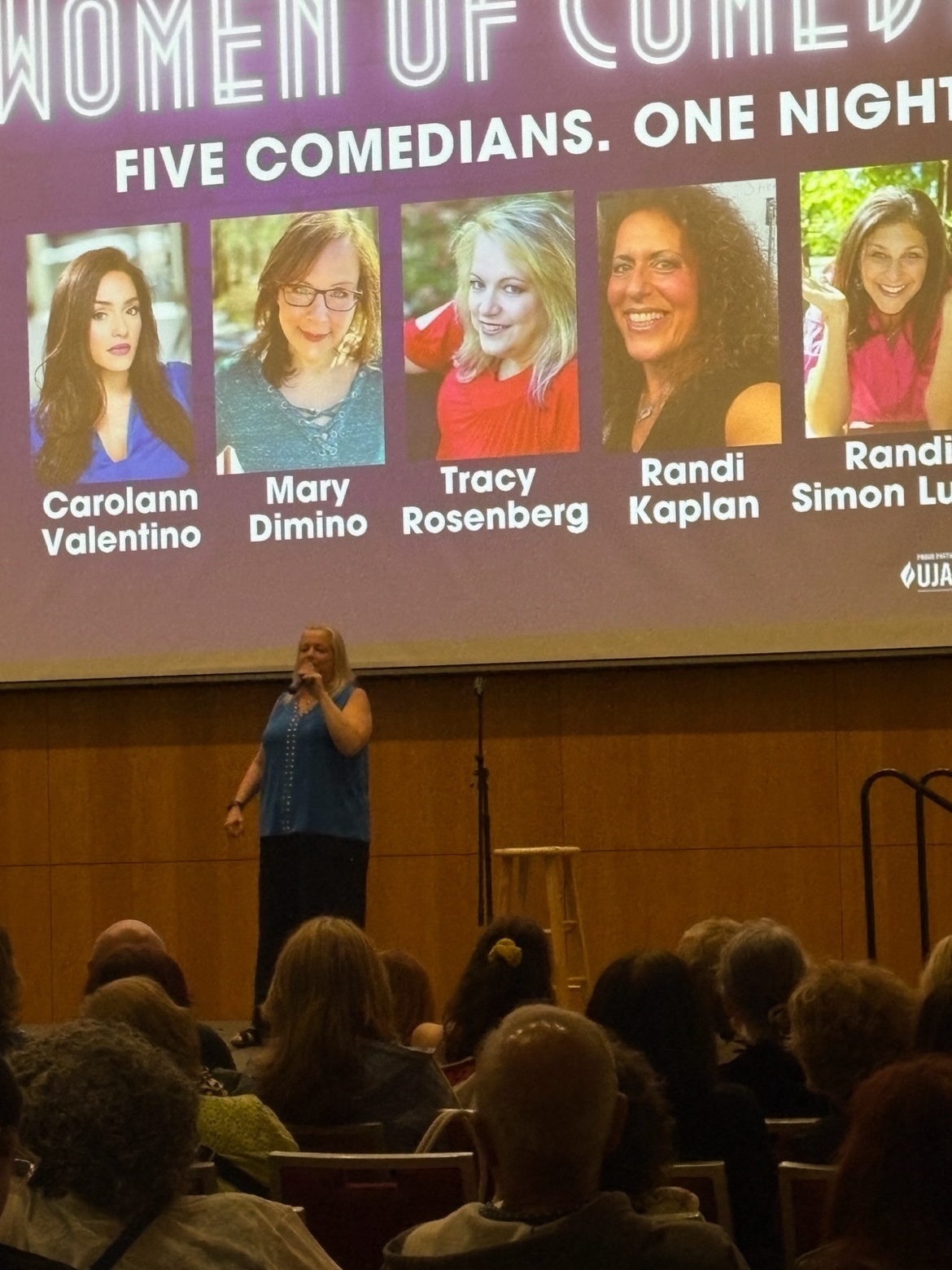 A comedian performing at the Grushkin Center with the Supersized Women of Comedy projection behind her